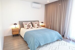 A modern bedroom with a bed, nightstands, a lamp, and a window with curtains. - Luxury 3-bedroom Privilege Casa do Colhereiro with Private Pool (Luz)