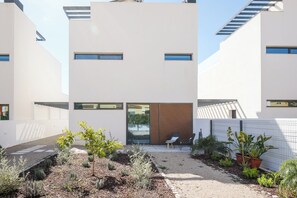 Un edifici modern amb una entrada central, diverses finestres i un camí de grava que condueix a una zona d'estar.