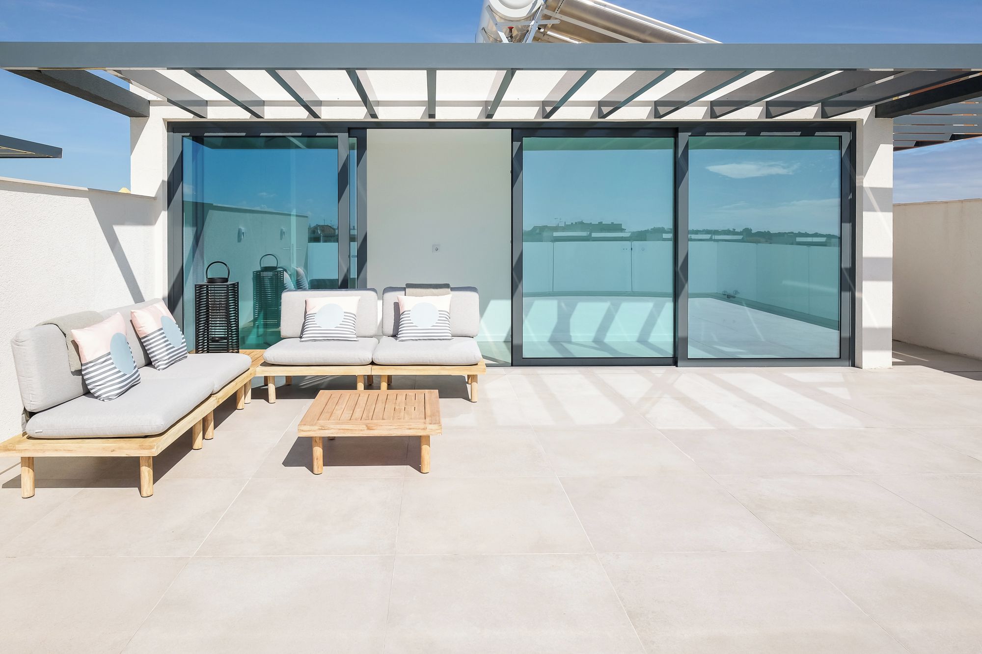 A modern outdoor seating area with a sofa and chairs, a wooden table, and a glass door leading to a balcony.