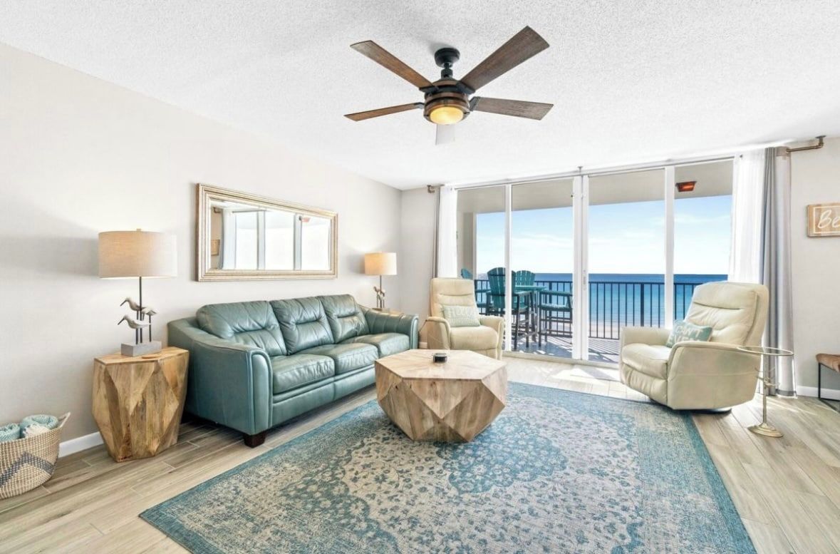 A spacious living room with a large window, a ceiling fan, and a view of the ocean.
