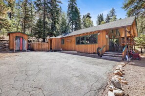 A wooden cabin with a large garage, a covered porch, and a fenced-in area with skis. - Bear Cub Ski Haus- Hot Tub- Near Bear Mt- Slps 5 (Big Bear Lake)