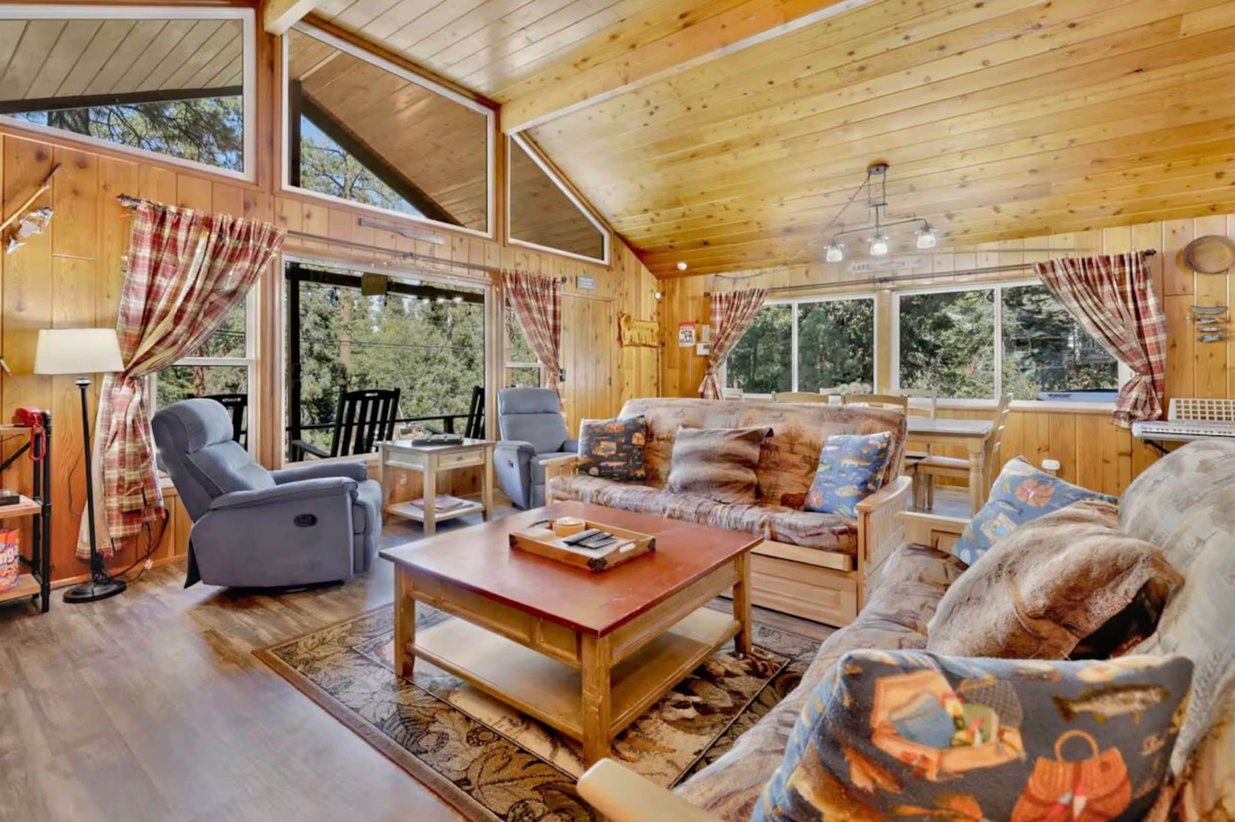 Een gezellig chaletinterieur met een bank, fauteuils, een eettafel en een groot raam met uitzicht op de omgeving.
