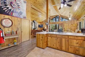 A wooden cabin interior with a kitchen area, a dining table, and a large window. - Bear Cub Ski Haus- Hot Tub- Near Bear Mt- Slps 5 (Big Bear Lake)