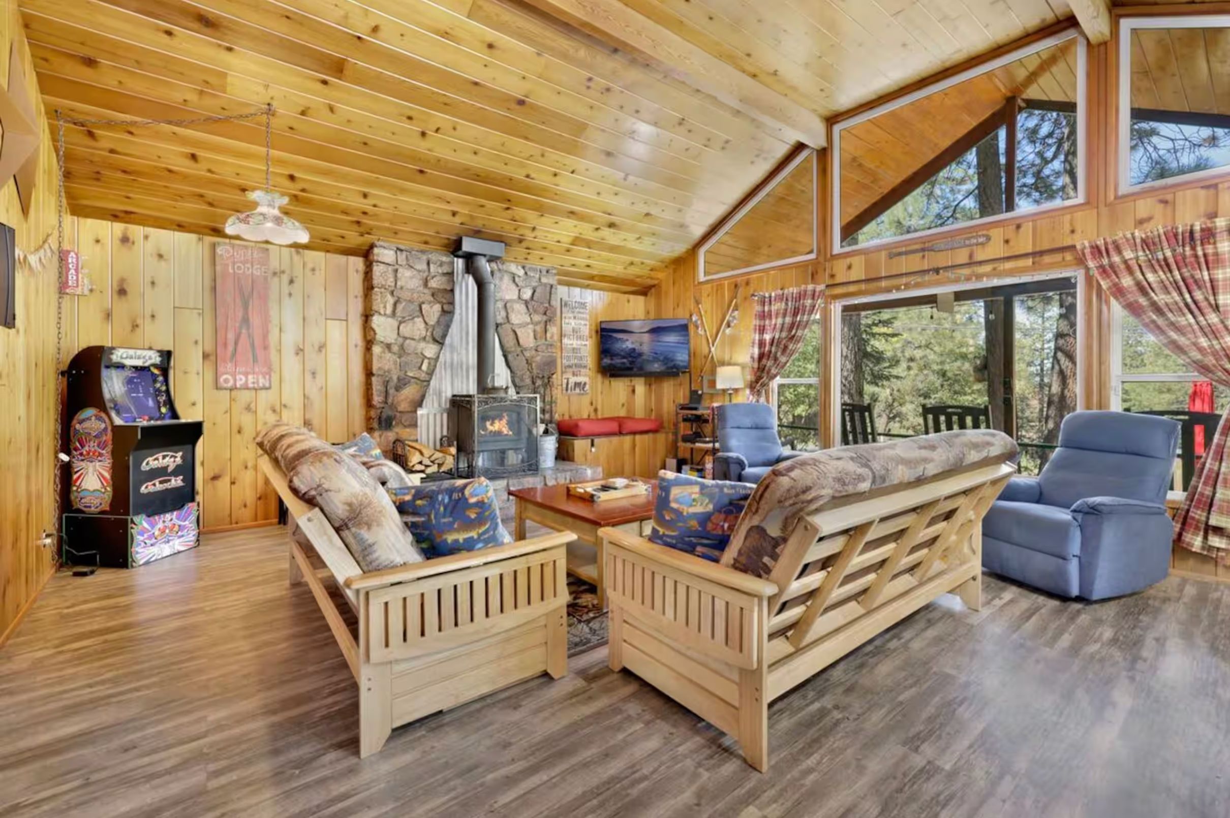 L’intérieur chaleureux d’un chalet avec une cheminée en pierre, des meubles en bois et une grande fenêtre donnant sur le paysage extérieur.