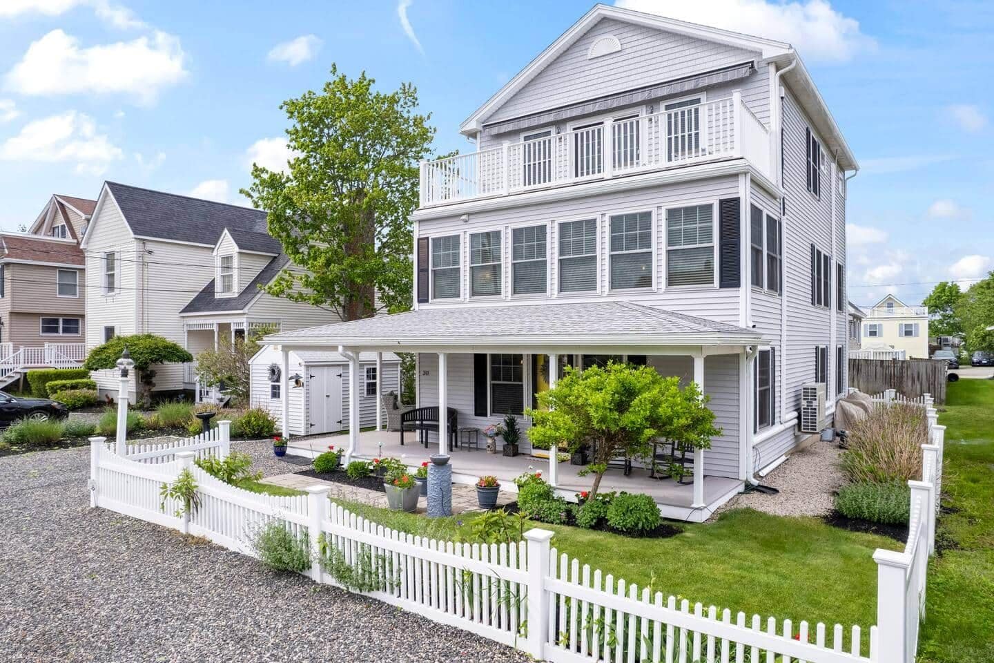 A two-story house with a covered porch, a fenced yard, and a gravel driveway.
