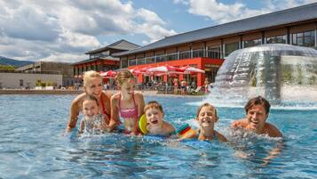 Ein Schwimmbecken mit darin befindlichen Personen, ein Gebäude mit roter Fassade und ein Wasserfall.