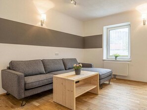 A modern living room with a grey sofa, a wooden coffee table, and a window with a view.