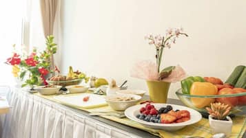 A breakfast buffet with various fruits, vegetables, and a vase of flowers.