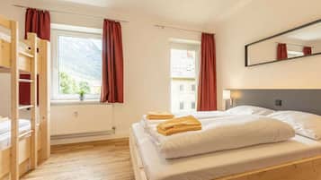 Ein Zimmer mit einem Bett, einem Holzschrank, einem Fenster mit Vorhängen und einem Spiegel an der Wand.