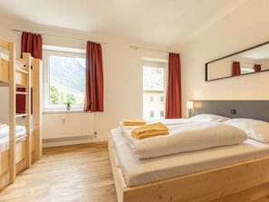 A room with a bed, a wooden wardrobe, a window with curtains, and a mirror on the wall.