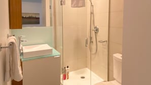 Un baño con ducha envuelta en vidrio, un lavamanos con encimera de vidrio y un inodoro.