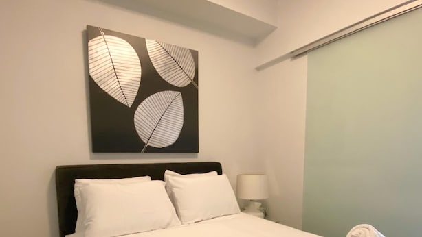 Una cama bien hecha con sábanas blancas, un cabecero y una obra de arte en la pared con motivos de hojas.
