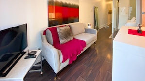 Una sala de estar moderna con un televisor de pantalla plana, un sofá con una manta roja y un cuadro abstracto grande en la pared.