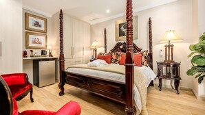 A four-poster bed with a wooden frame, a desk with a computer, a red chair, and a potted plant.