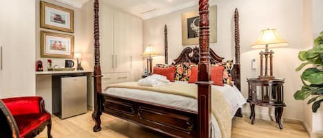 A four-poster bed with a wooden frame, a desk with a computer, a red chair, and a potted plant.