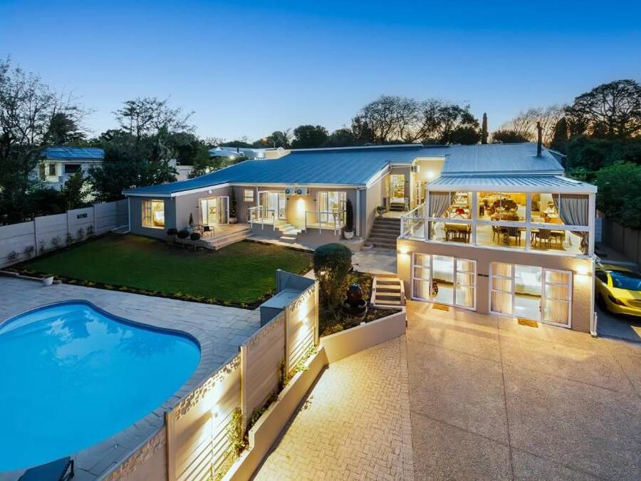 A two-story house with a swimming pool, a covered patio, and a yellow car parked outside.