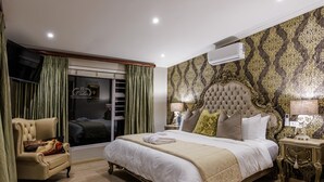 A spacious bedroom with a large bed, a chaise lounge, a vanity with a mirror, and a window with curtains.