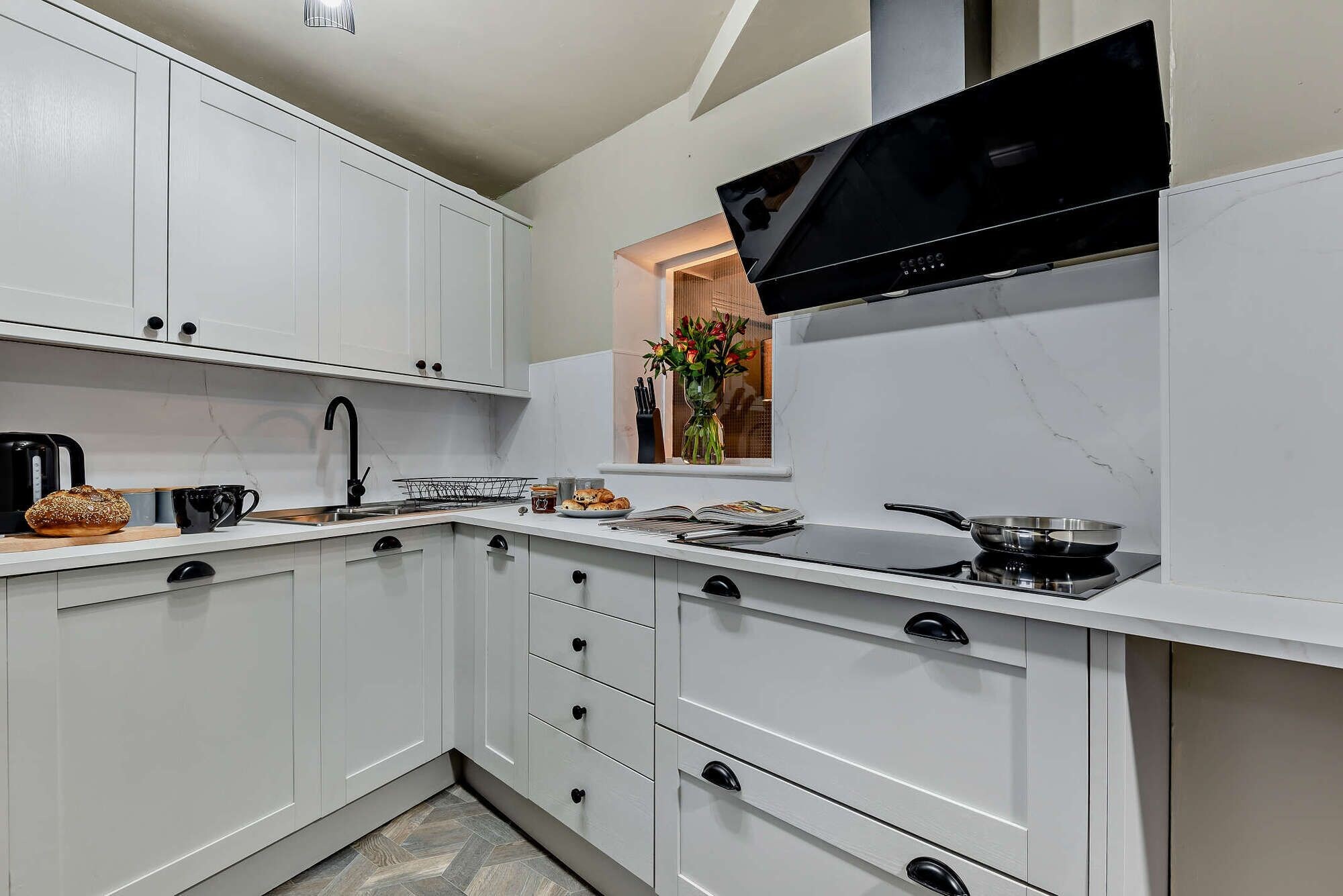 Une cuisine moderne avec des meubles blancs, une cuisinière noire et une fenêtre donnant sur une plante.