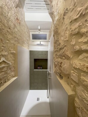 A narrow shower with stone walls, a white ceiling, and a built-in shelf with toiletries. - Vrbo Property (Locorotondo)