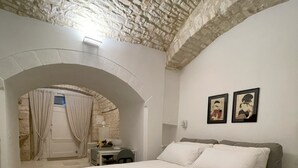 Quarto com teto de pedra, uma cama, uma escrivaninha com cadeira e duas fotografias emolduradas na parede.