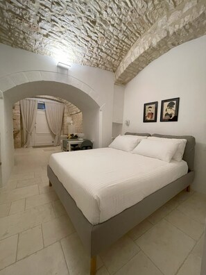 A bedroom with a stone ceiling, a bed, a desk with a chair, and two framed pictures on the wall. - Vrbo Property (Locorotondo)