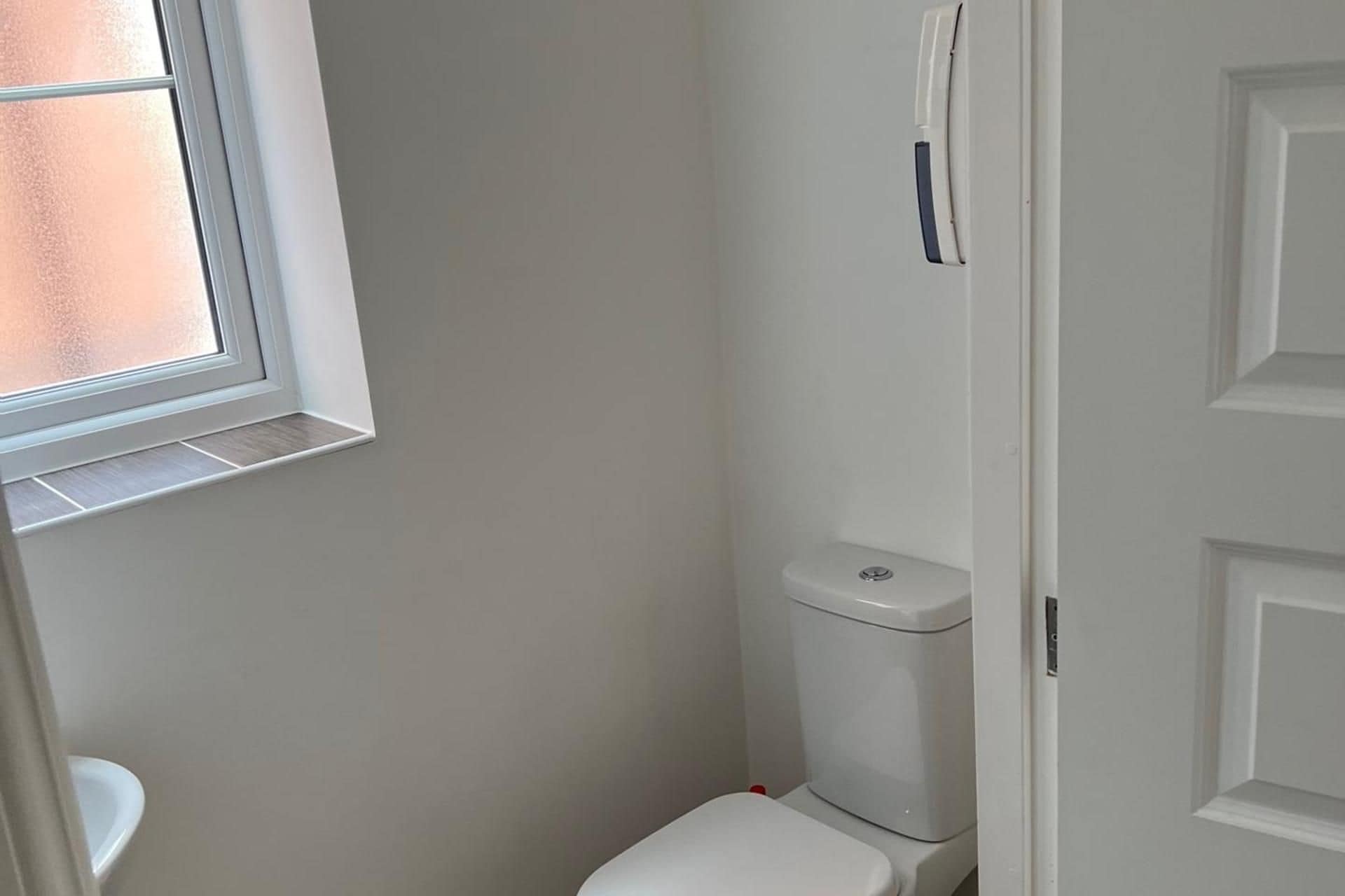 A small, narrow bathroom with a toilet, a window, and a door.