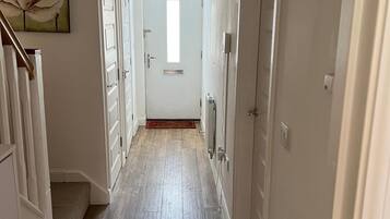 A hallway with a wooden floor, white doors, and a door at the end leading to a room.