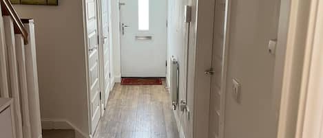 A hallway with a wooden floor, white doors, and a door at the end leading to a room.
