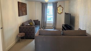 Een woonkamer met een bank, een televisie, een schilderij en een raam met gordijnen.
