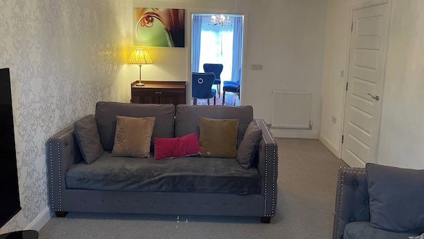 Een woonkamer met een grijze bank, een lamp, een schilderij en een kroonluchter.