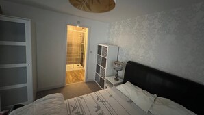 Een slaapkamer met een bed, een kledingkast, een nachtkastje, een lamp en een badkamer met douche.
