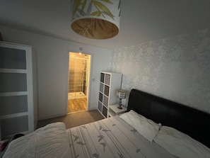 Une chambre à coucher comprenant un lit, une armoire, une table de chevet et une lampe, ainsi qu’une salle de bain avec douche.