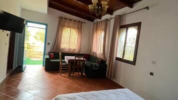 A bedroom with a large bed, wooden ceiling beams, a desk with a chair, and a window.