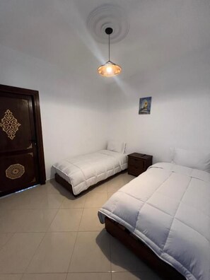 Un dormitorio con dos camas, una mesita de noche, una lámpara de pared y una puerta con panel decorativo.