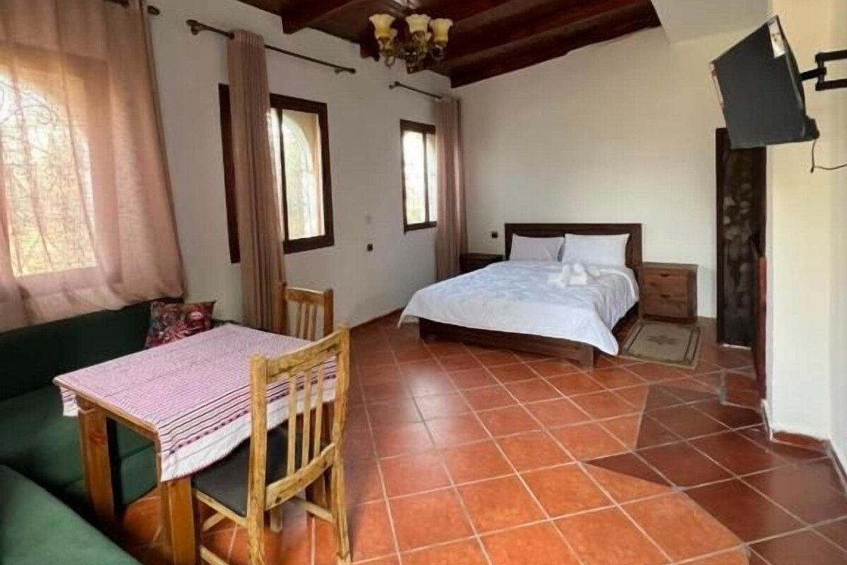 A room with a bed, a table with chairs, a green sofa, and a tiled floor.