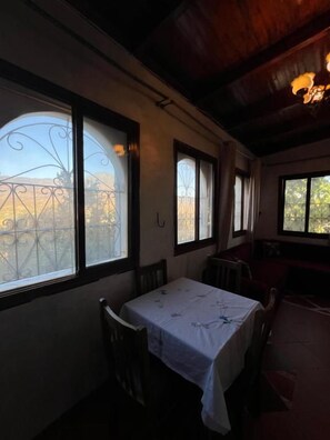 Un comedor con mesa y sillas, ventanas amplias con vistas y techo de madera.