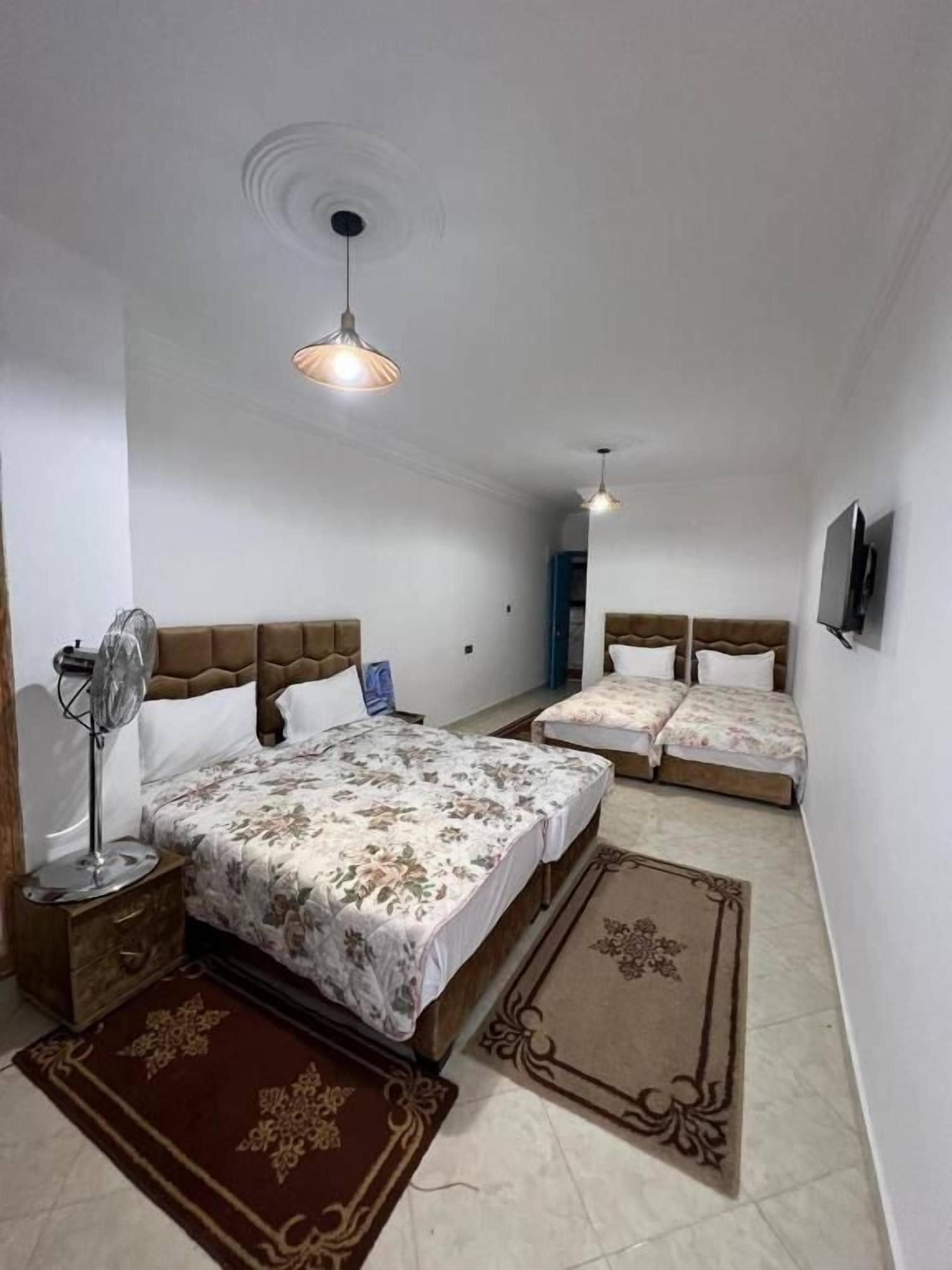 A bedroom with a large bed, two smaller beds, a ceiling fan, a TV, and a door leading to another room.