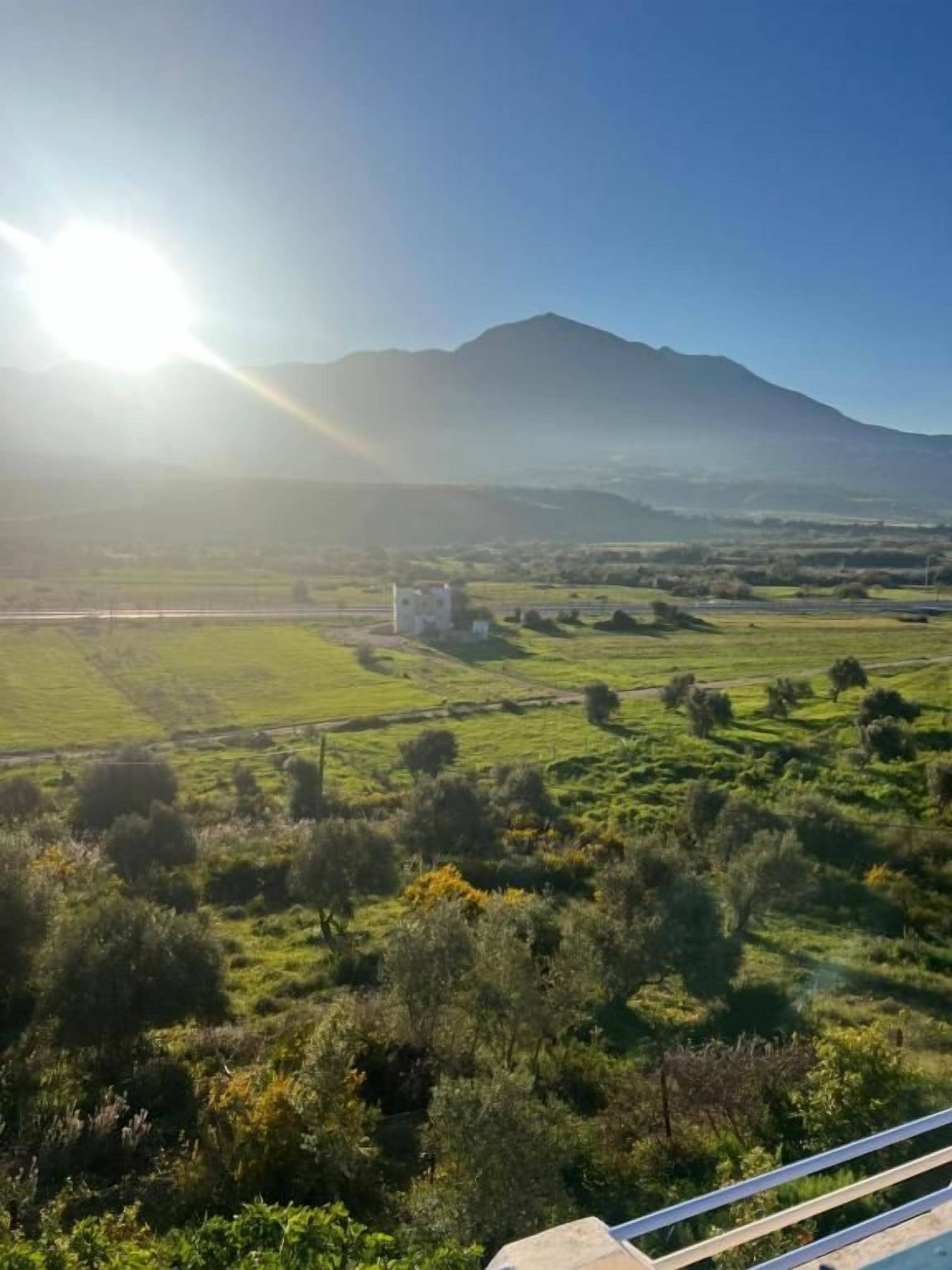 A rural landscape with a mountain in the background, a clear sky, and a building in the foreground.