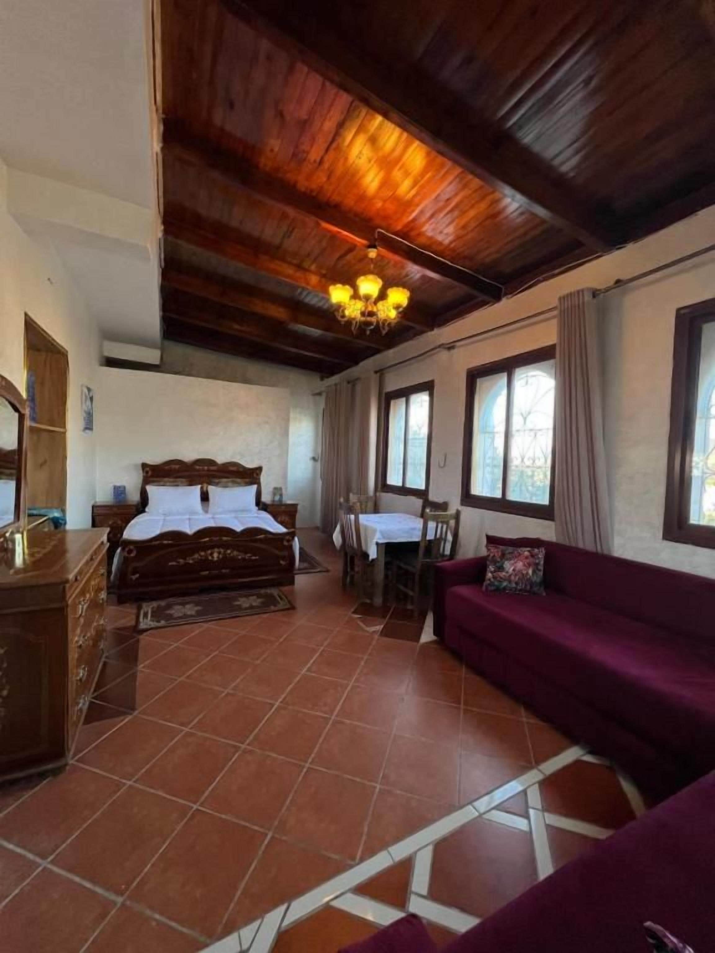 Una habitación con techo de madera, una cama con cabecera, un sofá, una mesa y una silla.