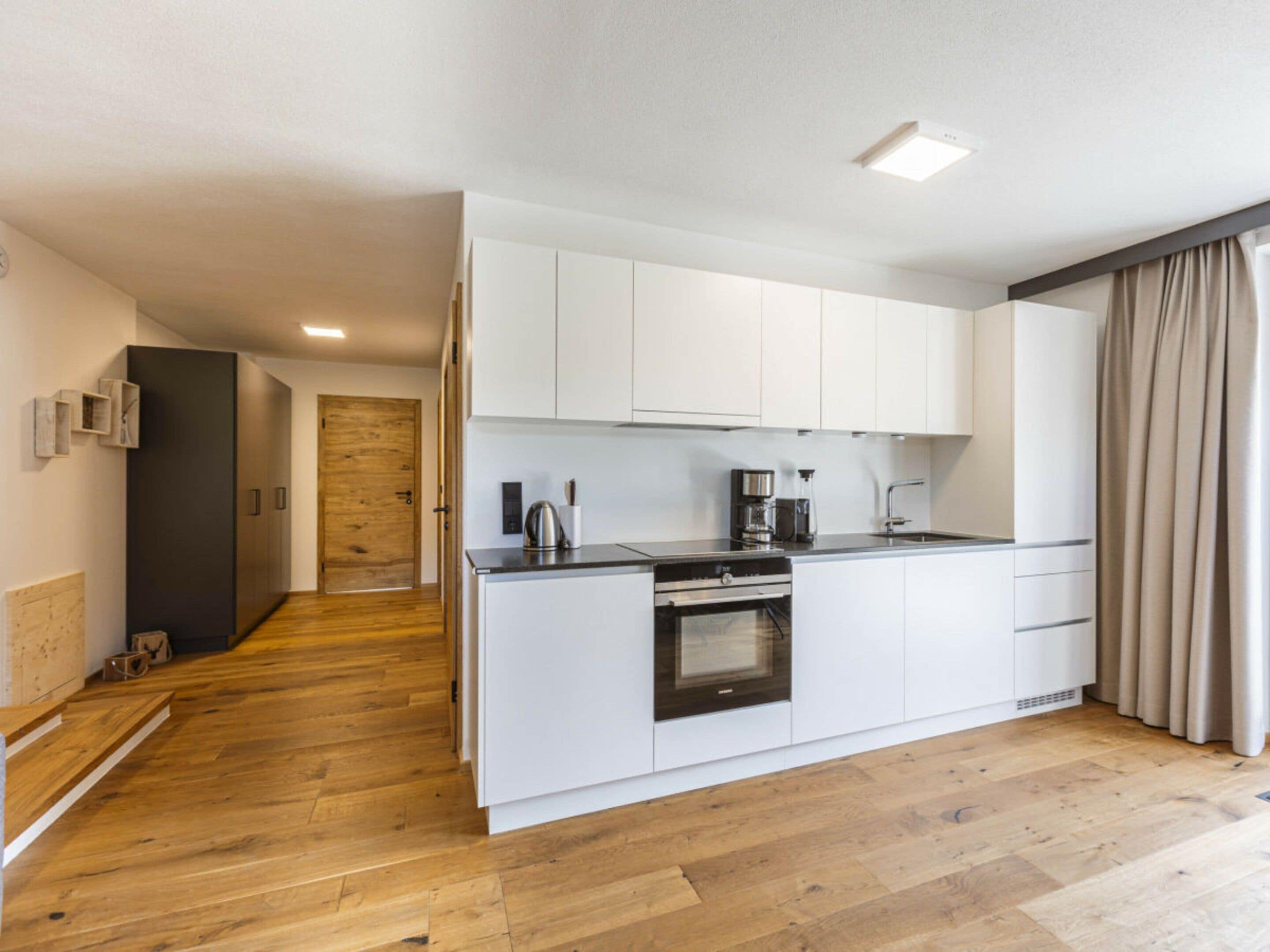 A modern kitchen with white cabinets, a built-in oven, and a coffee maker.