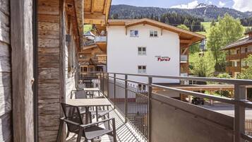 A wooden balcony with a table and chairs, overlooking a mountain landscape and a hotel building with 'APART HOTEL Tyrol' signage.