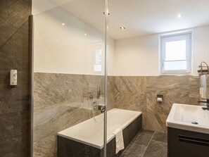 Un baño moderno con ducha envuelta en vidrio, bañera independiente y tocador con lavamanos.