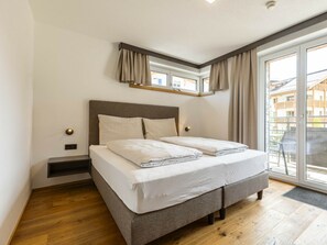 Un dormitorio con cama, mesita de noche, ventana con cortinas y vistas a edificios.