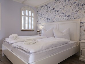 Ein Doppelbett mit weißen Leinen und Kissen, ein Nachttisch mit Lampe und ein Fenster mit Rollläden.