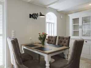 En spiseplads med et bord, stole, en vase med blomster og et skab med glasdøre.