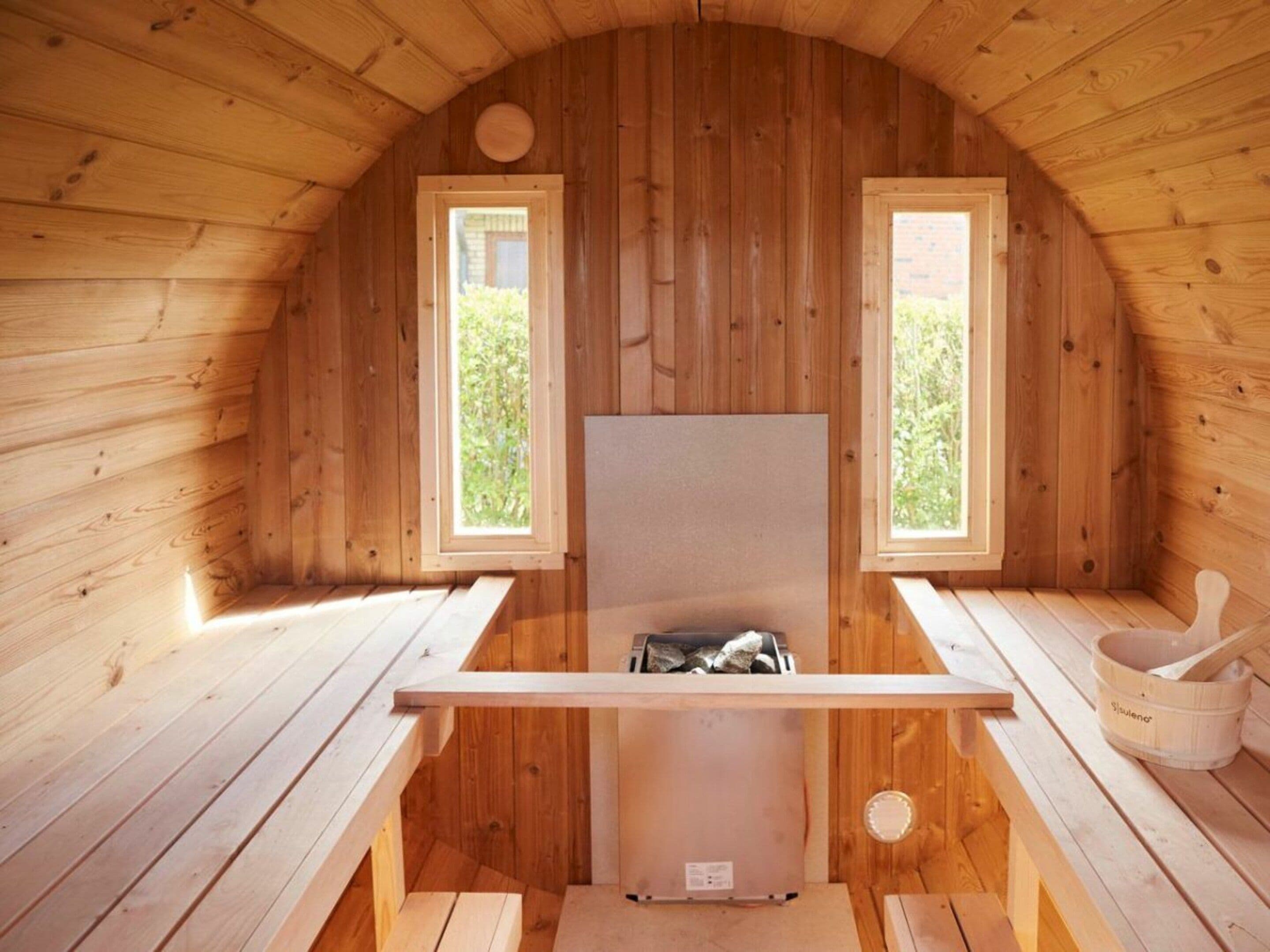 A wooden cabin with two windows, a fireplace, and a wooden bench.