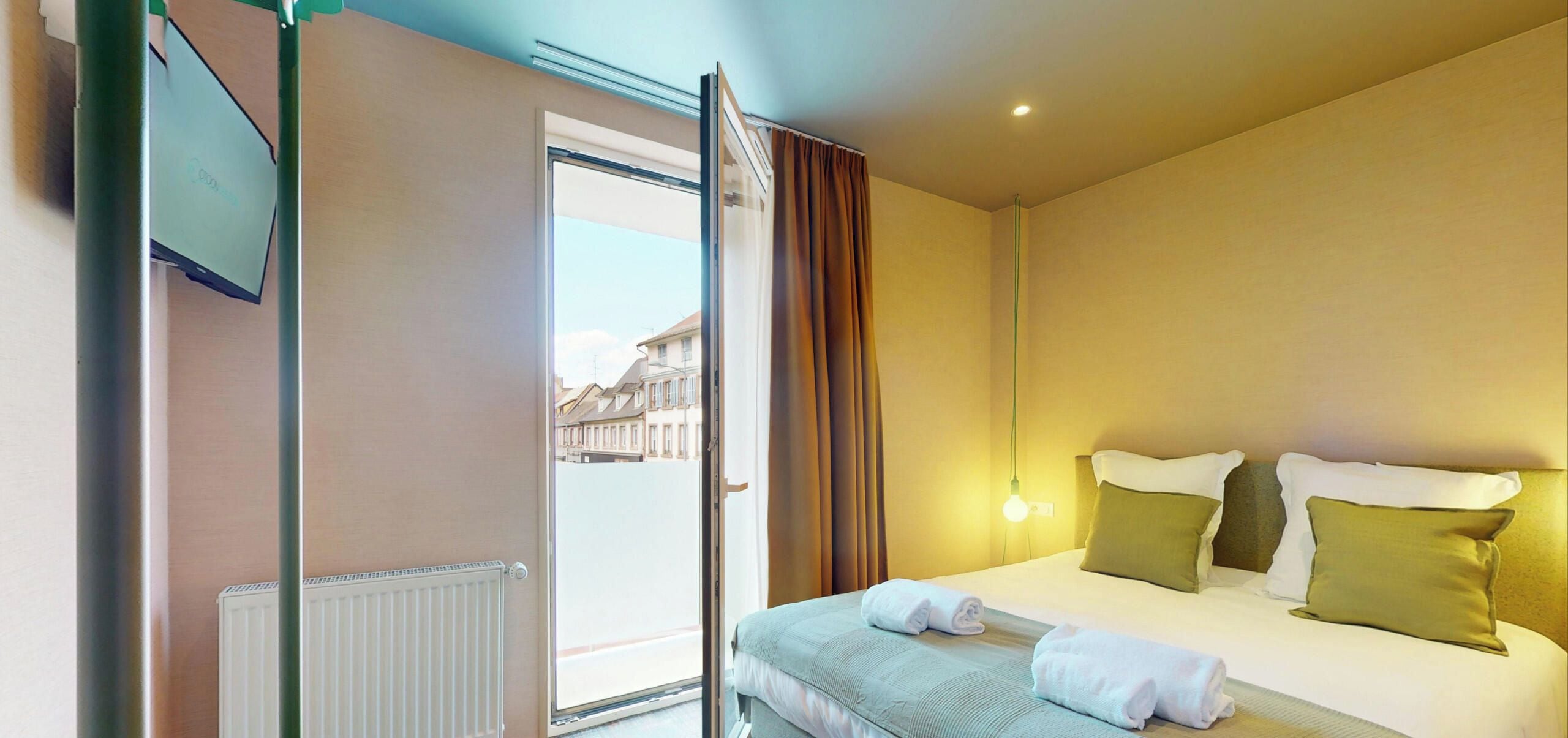 Ein Hotelzimmer mit einem Bett, einem Heizkörper, einem fenster mit Vorhängen und Blick auf Gebäude.