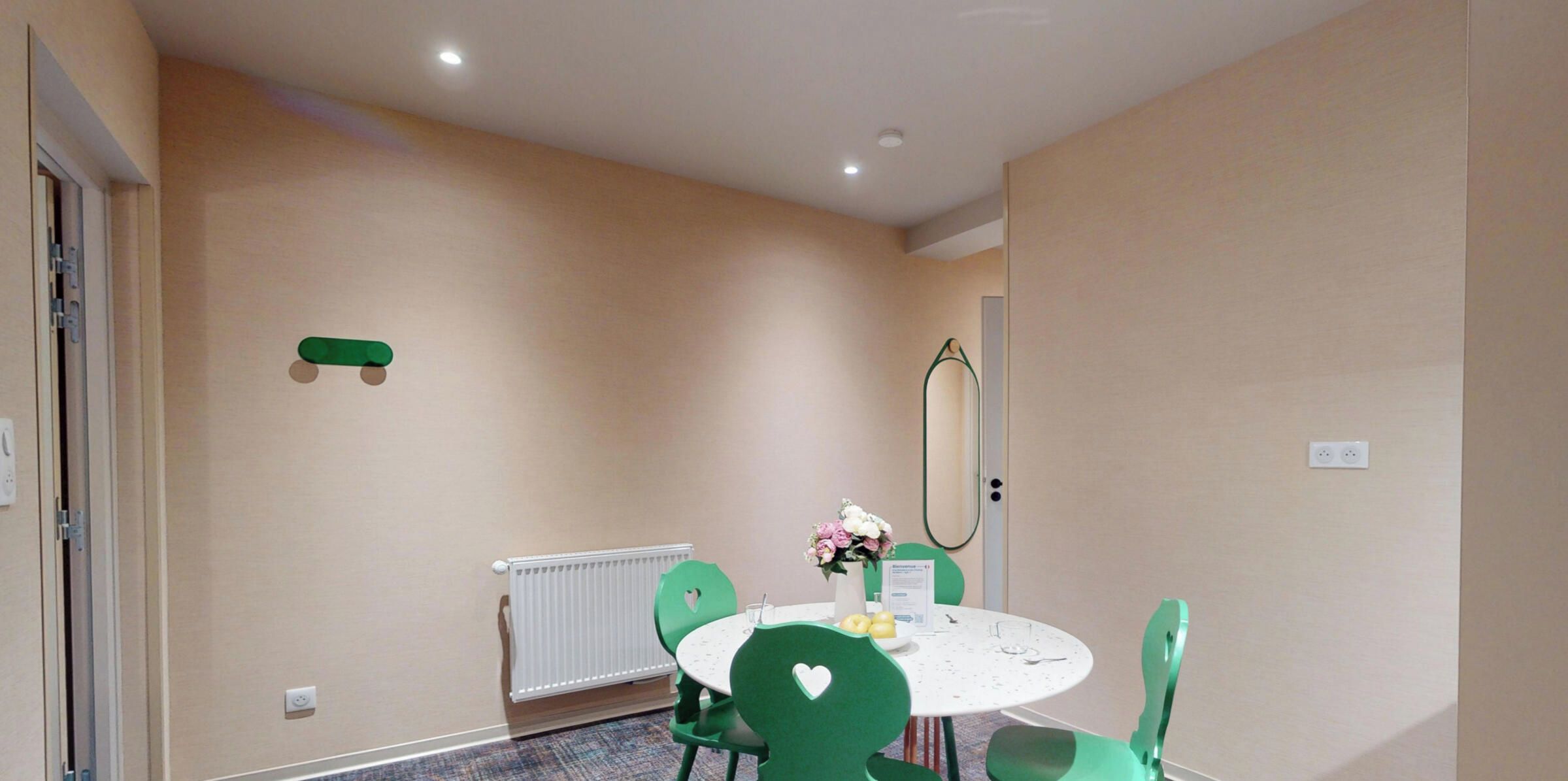 A room with a round table, green chairs, a radiator, a mirror, and a door.