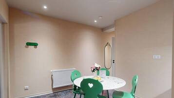 A room with a round table, green chairs, a radiator, a mirror, and a door.