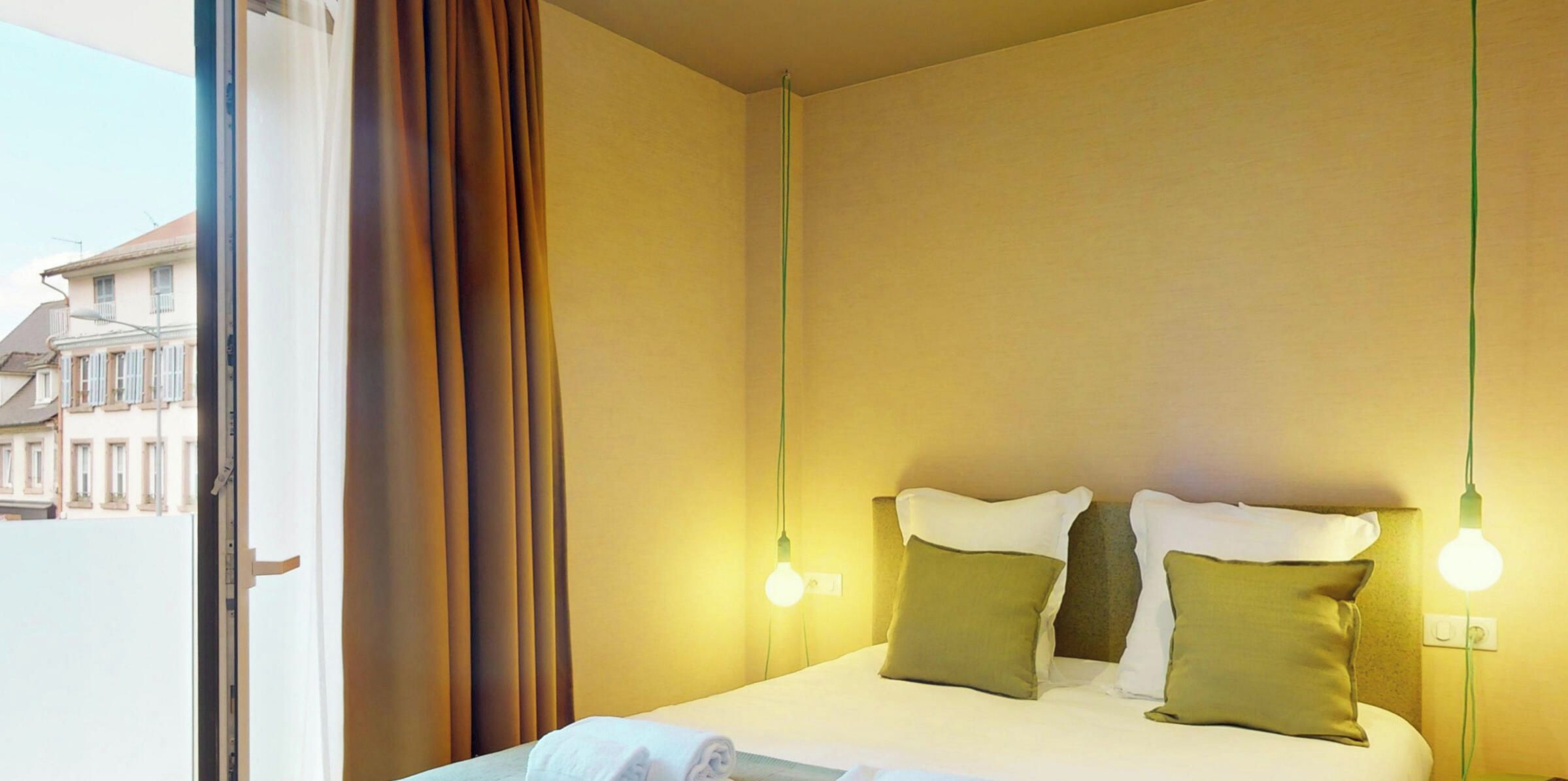 A hotel room with a bed, curtains, and two wall-mounted lights.